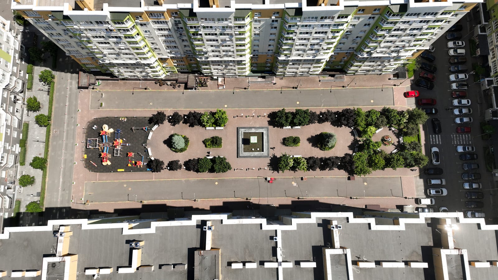 A closed courtyard of a SAVO district straight from above: playground, planted islands, a square with water and the parking outside